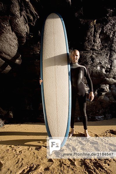 Mann steht mit lächelndem Surfbrett.
