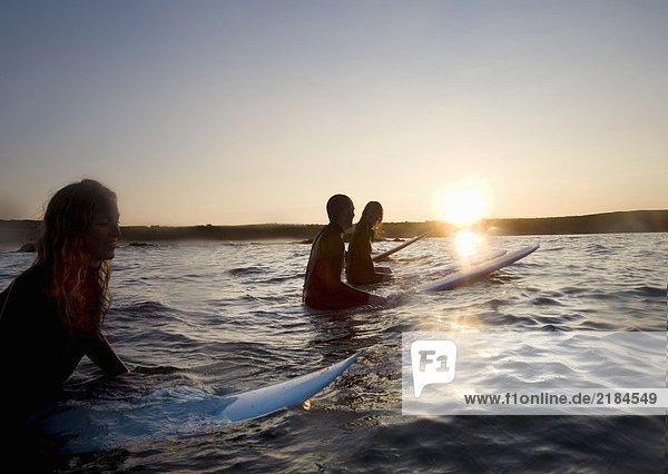 Vier Leute sitzen auf Surfbrettern im Wasser und lächeln.