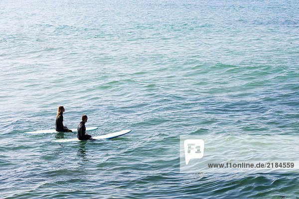 Couple sitting on surfboards in the water.
