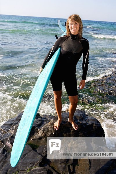 Frau stehend mit einem Surfbrett lächelnd.