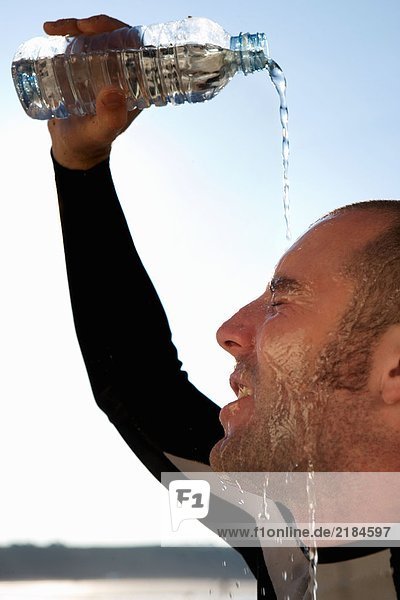 Ein Mann im Neoprenanzug schüttet Wasser auf sein Gesicht.