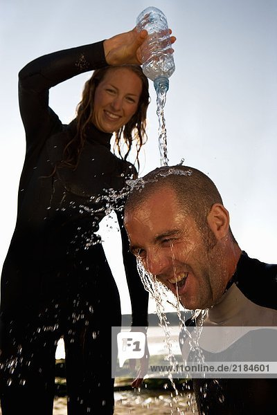 Frau gießt Wasser über den Kopf des lachenden Mannes.