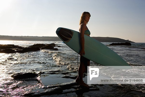 Frau steht im flachen Wasser mit Surfbrett.