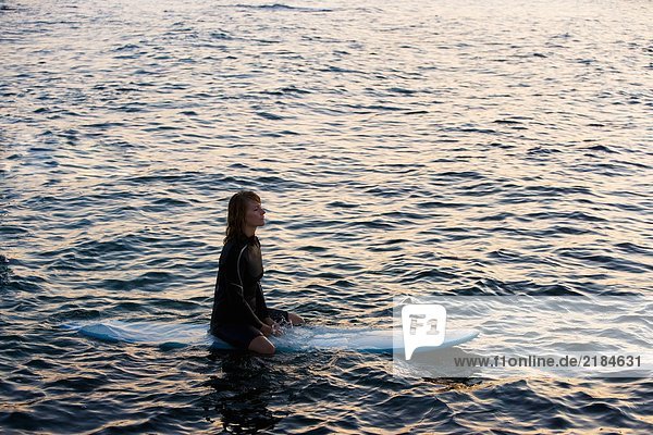 Frau sitzt auf dem Surfbrett im Wasser.