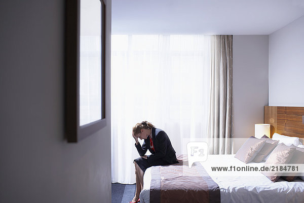 Woman sitting on edge of bed with head in hands