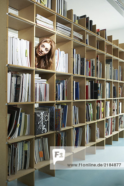 Frau spannt Kopf durch Bücherregal