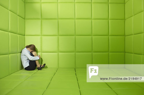 Frau in einer Ecke in einer grün gepolsterten Zelle geduckt