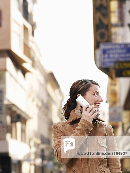 Young woman standing in street using mobile phone  smiling