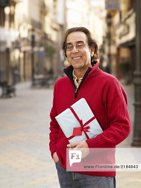 Mature man standing in street holding gift  smiling  portrait