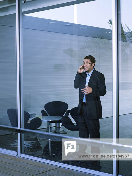 Young businessman standing at office window using mobile phone