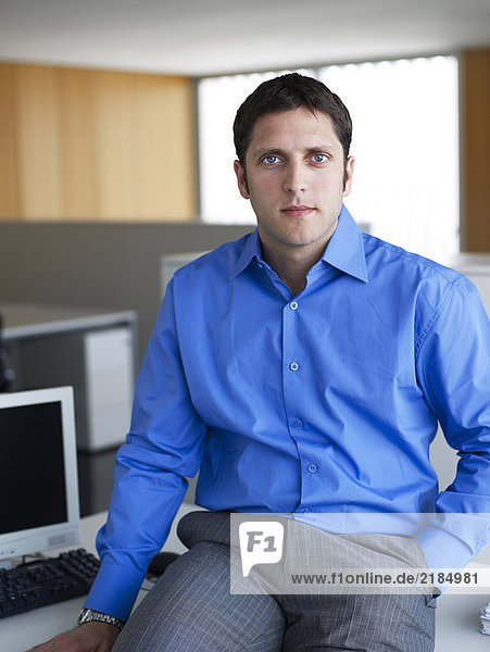 Young businessman sitting on desk in office  portrait