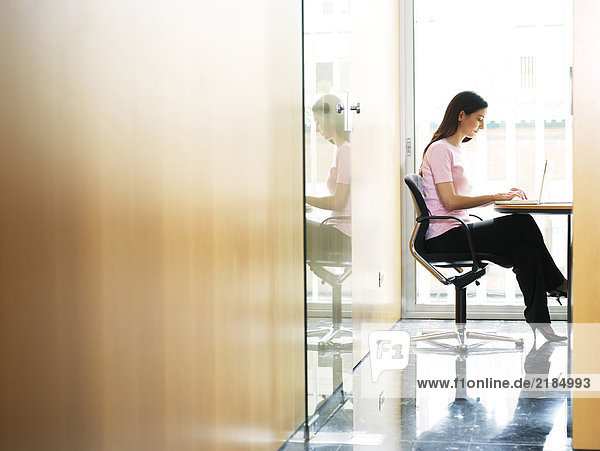 Junge Geschäftsfrau im Büro sitzend mit Laptop  Seitenansicht