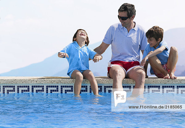 Vater sitzend am Schwimmbad mit zwei Söhnen (5-7)
