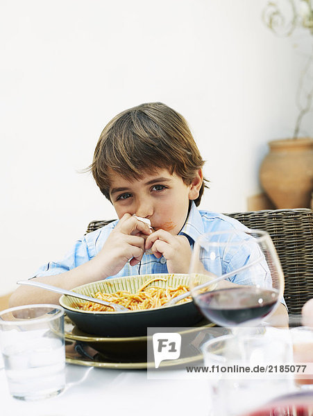 Junge (4-6) isst Spaghetti beim Mittagessen im Garten  Portrait