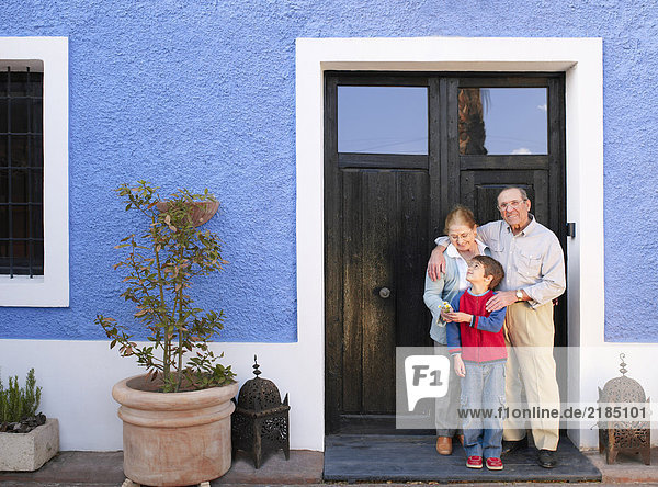 Großeltern und Enkel (6-8) vor der Haustür stehend  lächelnd