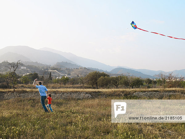 Father and son (4-6) running in a field with kite