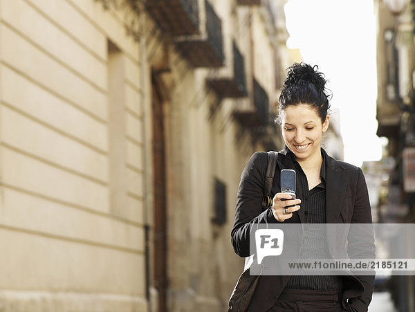 Young woman walking in street using mobile phone  smiling