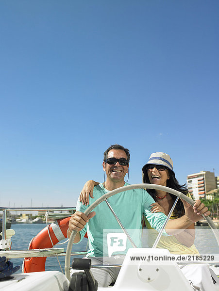 Erwachsenes Paar mit Sonnenbrille am Steuer der Yacht  lächelnd
