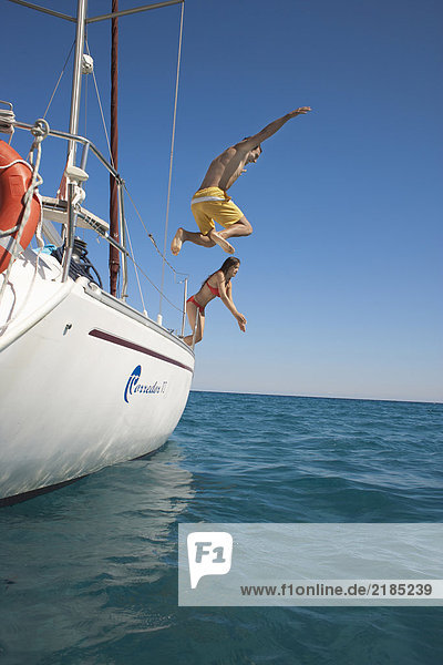 Young couple jumping off yacht into sea