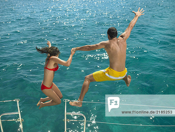 Couple jumping into sea from boat  rear view