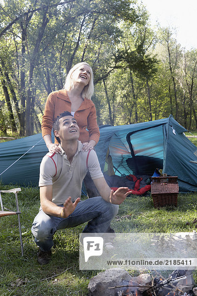 Ein Paar auf dem Campingplatz schaut lächelnd auf den Rauch der Feuerstelle.