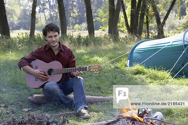 Man at campsite playing guitar and smiling.