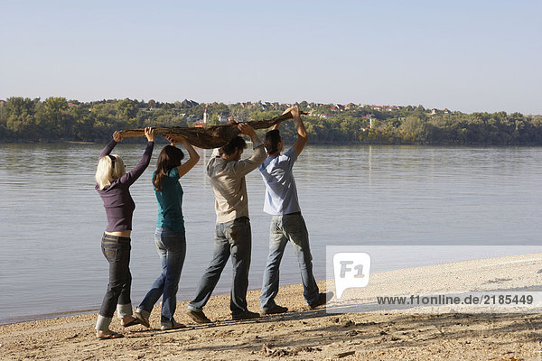 Vier Freunde mit einem Baumstamm am See.