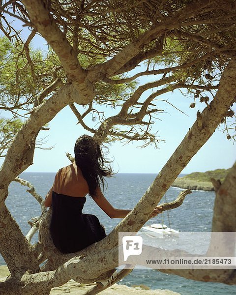 Eine Frau sitzt auf einem Baum mit einer vorbeifahrenden Jacht.
