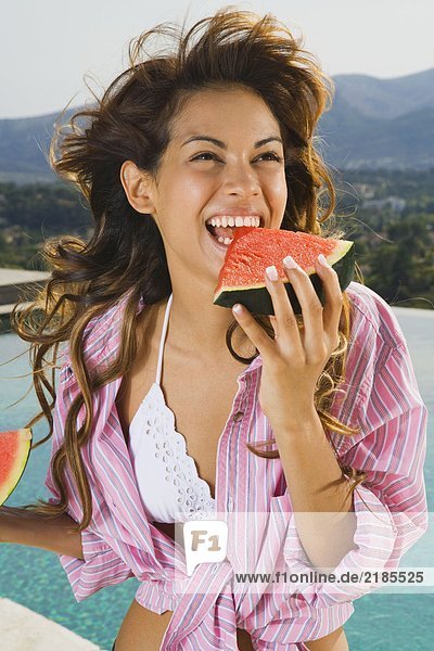 Energetische Frau mit Lächeln isst Wassermelone am Pool draußen.