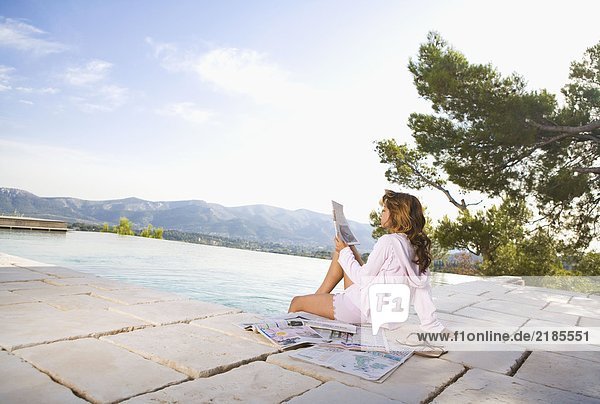 Frau entspannt sich bei unendlichem Pool und liest Zeitung.
