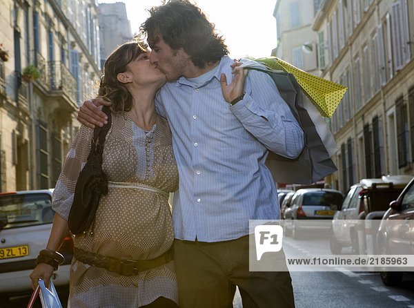 Schwangere junge Frau und junger Mann küssen sich auf der Straße.