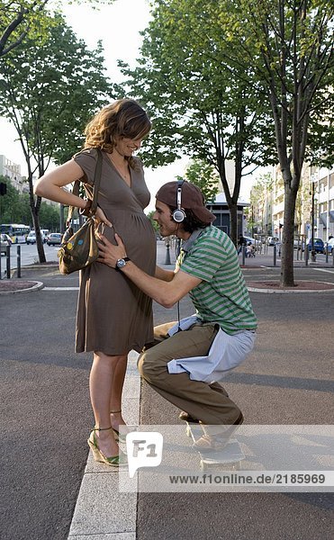 Young man crouching at pregnant young woman's stomach  smiling