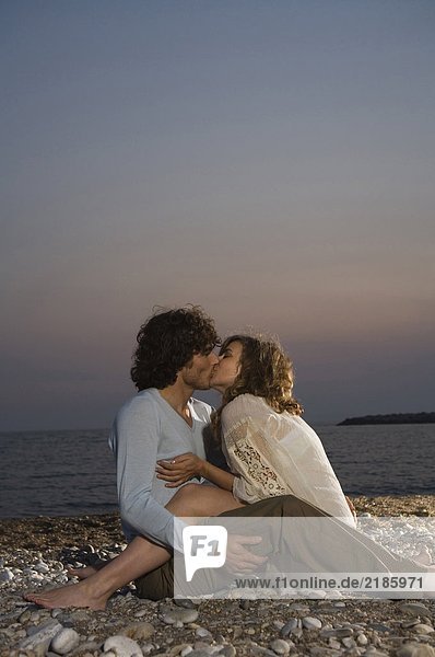 Young couple sitting on beach kissing  sunset