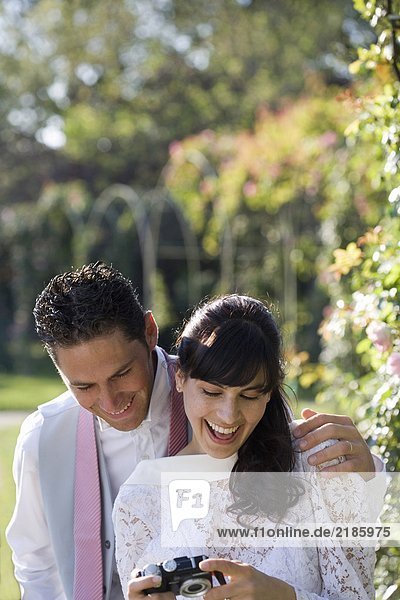 Junge Braut und Bräutigam mit Blick auf die Digitalkamera im Garten  lächelnd