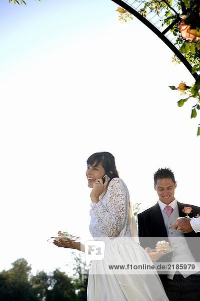 Junge Braut mit Handy  Bräutigam im Hintergrund  Lächeln