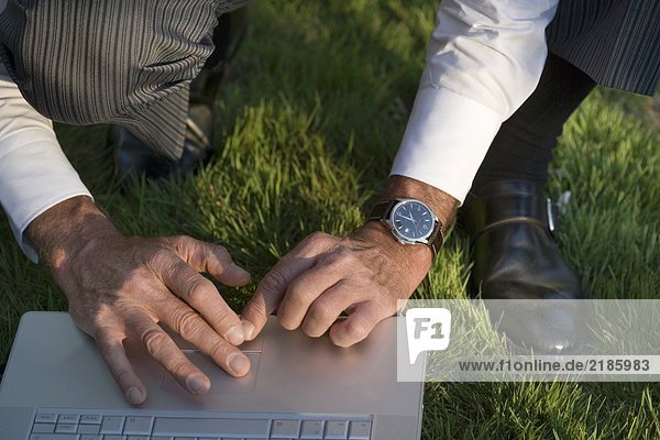 Mann hockt auf Gras mit Laptop  Nahaufnahme