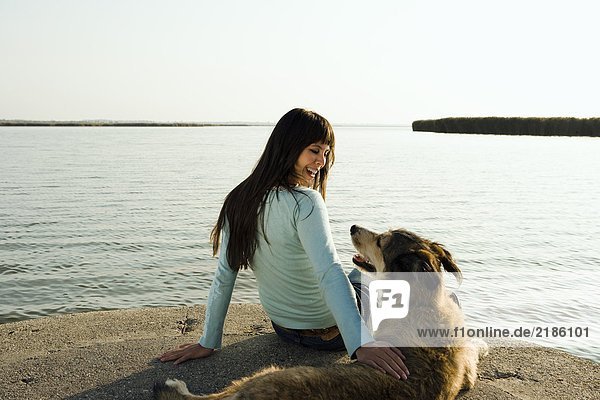 Frau am See sitzend mit Hund.