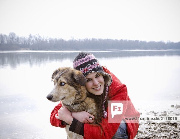 Junge Frau kniend am Fluss umarmend Hund  lächelnd  Portrait