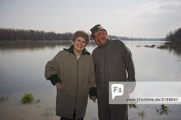 Senior couple standing by river  holding hands  smiling  portrait