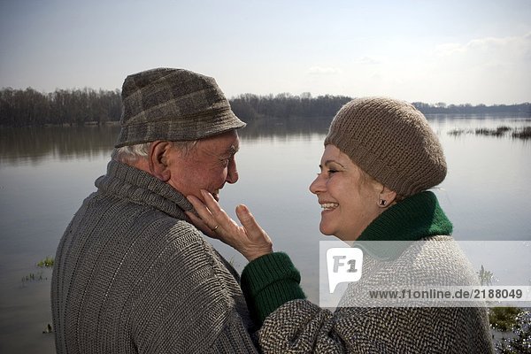 Seniorenpaar am Fluss  Frau berührt das Gesicht des Mannes  lächelnd