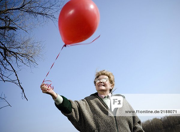 Senior woman outdoors holding red balloon  smiling  low angle view
