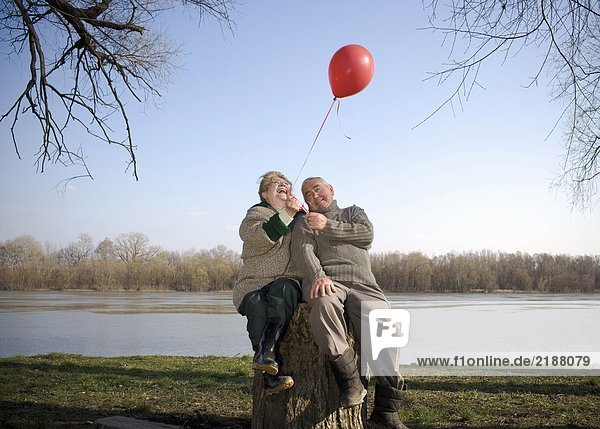 Senior couple sitting by river holding red balloon  smiling