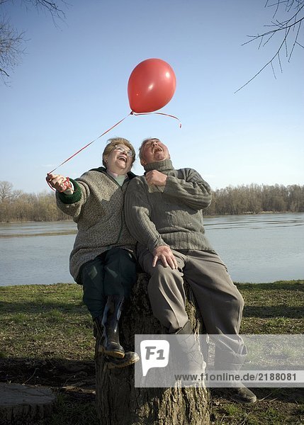 Senior couple sitting by river holding red balloon  smiling