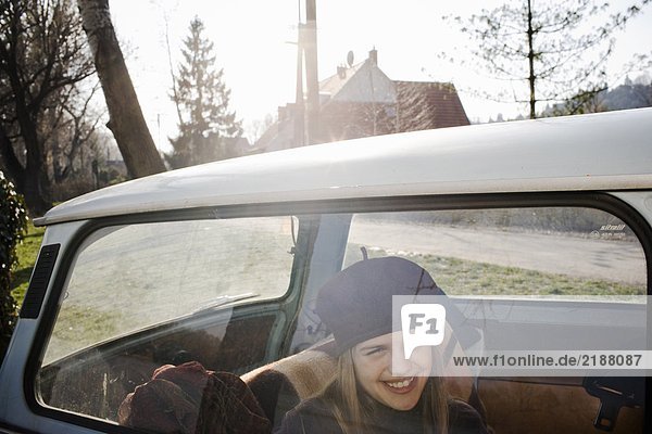 Girl (10-12) sitting in back of car  smiling  view through window