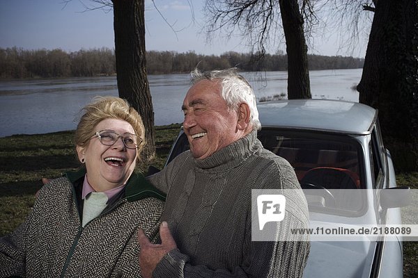 Senior couple standing by car on riverside  laughing