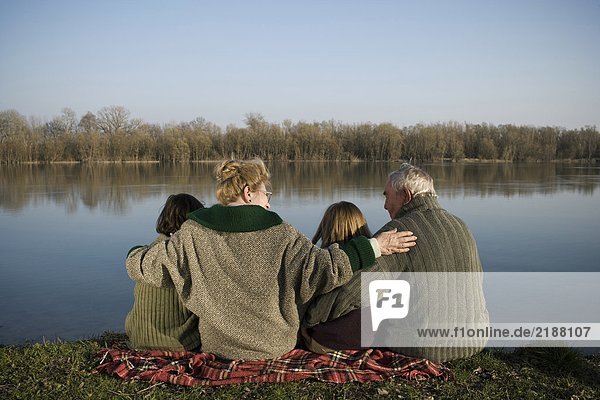 Grandparents  grandson (12-14) and granddaughter (10-12) sitting by river  rear view