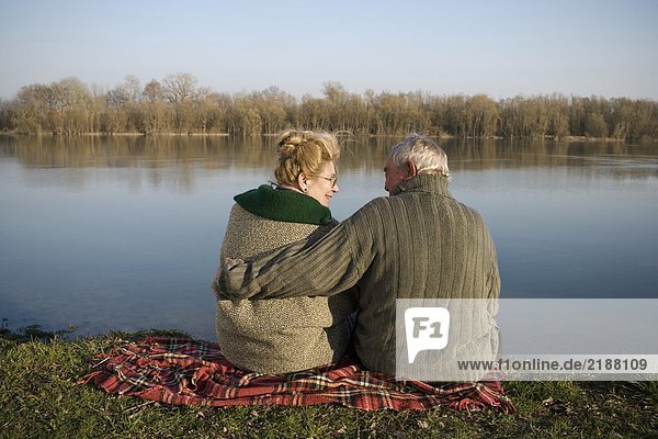 Senior couple sitting on rug by river  rear view  woman smiling