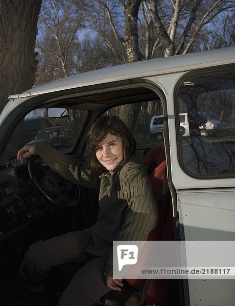Boy (12-14) sitting in driver's seat of car  smiling  portrait