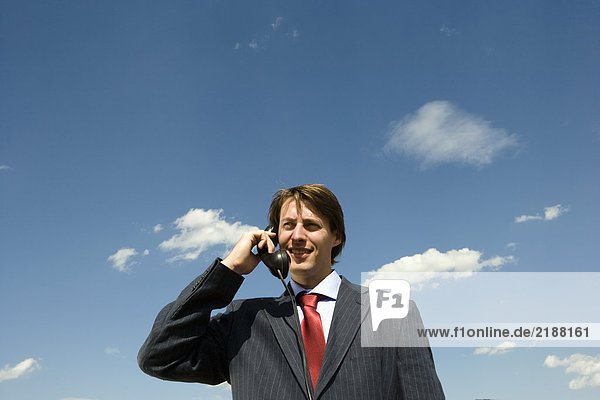 Mann hält altes Telefon gegen blauen Himmel.
