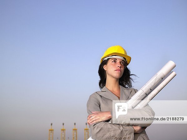 Frau mit Schutzhelm hält Entwürfe mit Türmen im Hintergrund.